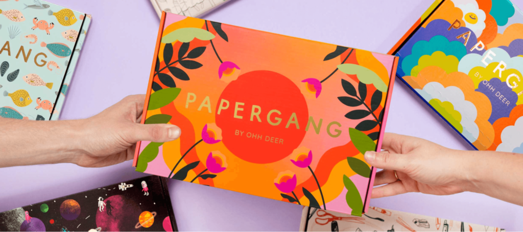 Two hands holding a box with the Papergang logo on it surrounded by other designed boxes on the table.