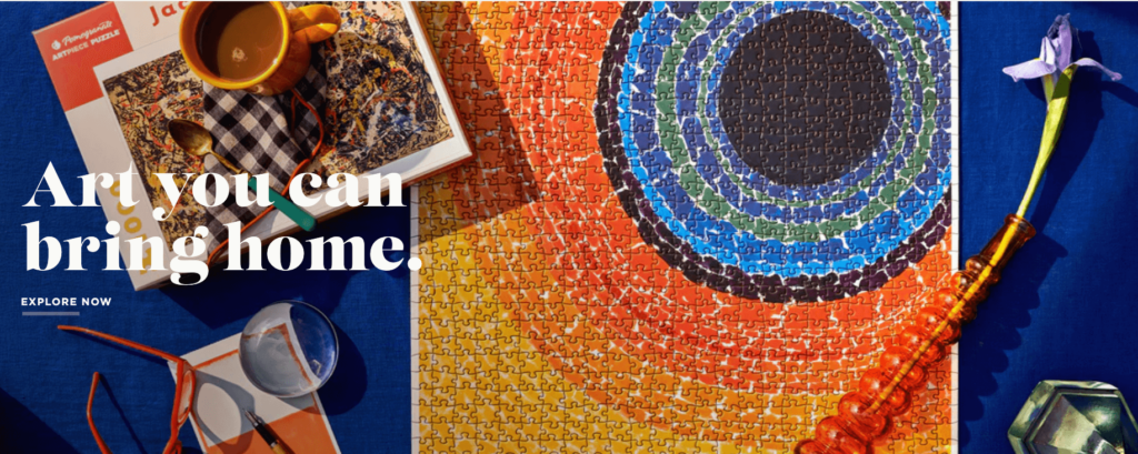 From Pomegrante's About Us page, a finished puzzle made up of beautiful pieces of rich yellows oranges and red on top of a blue blanket 